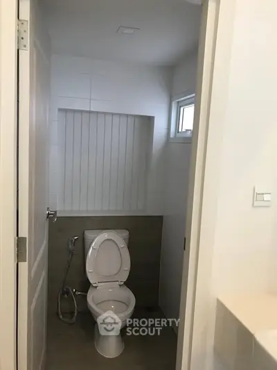 Modern bathroom with sleek design and compact layout, featuring a toilet and small window for natural light.