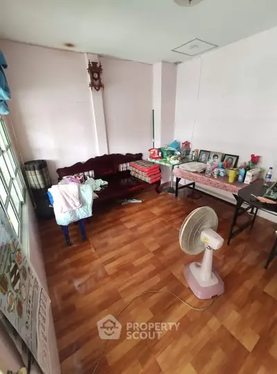 Cozy living room with wooden flooring and simple decor, featuring a fan and family photos.