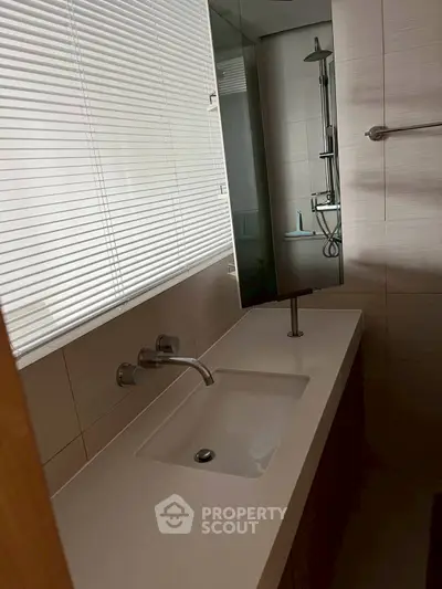 Modern bathroom with sleek sink and shower area, featuring contemporary fixtures.