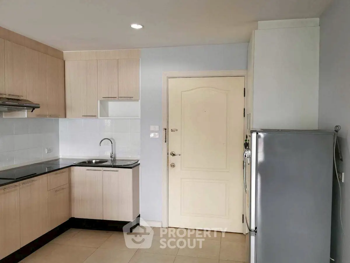 Modern kitchen with sleek cabinetry and stainless steel fridge in a cozy apartment.