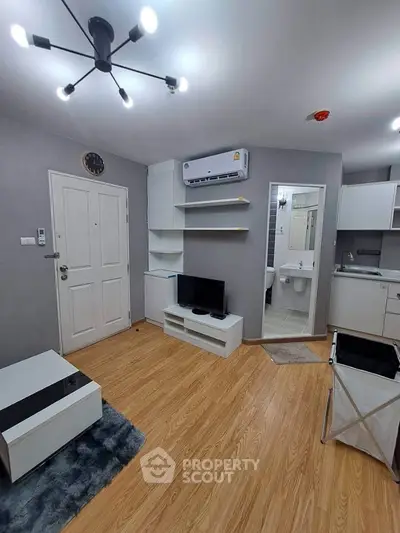 Modern living room with sleek design, featuring wooden flooring, wall-mounted TV, and compact kitchen area.