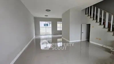 Spacious modern living room with glossy tiled floors and staircase, ideal for family gatherings.