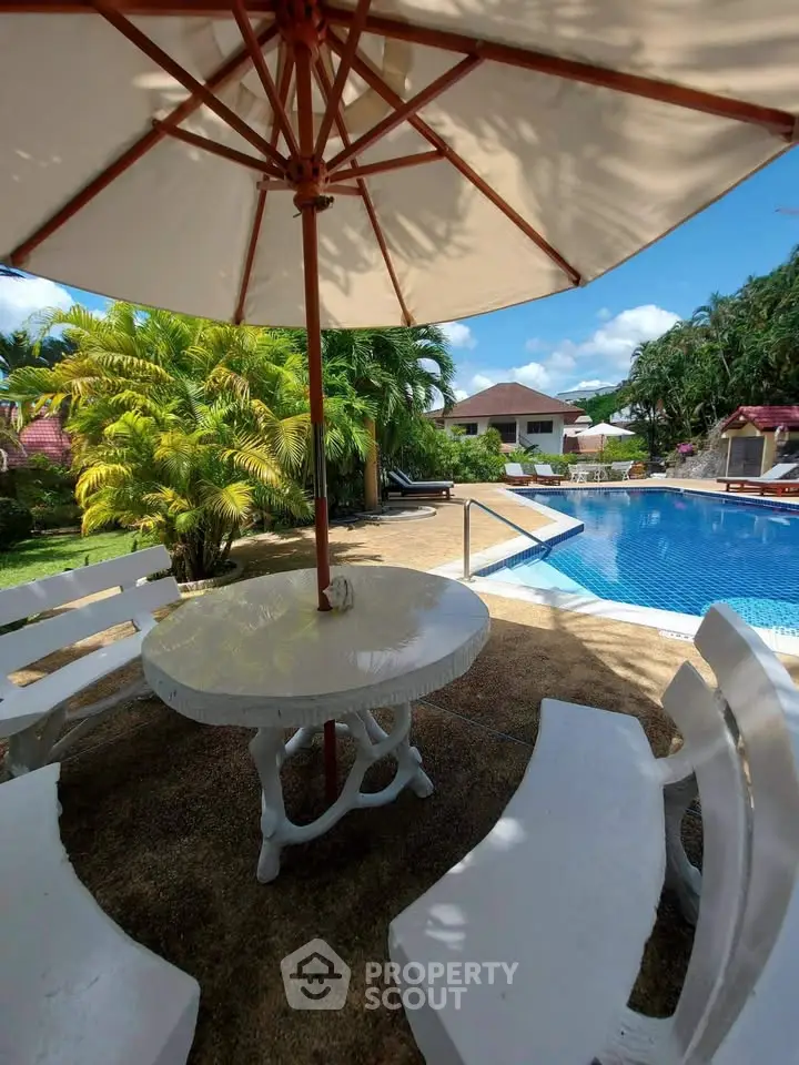 Luxurious poolside area with umbrella and seating, perfect for relaxation in a tropical setting.