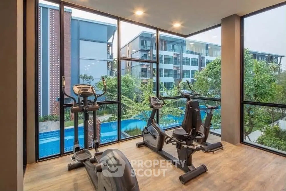 Modern gym with exercise equipment overlooking a scenic pool and garden view in a luxury apartment complex.