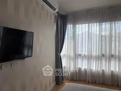 Bright bedroom with large windows and wall-mounted TV, featuring modern curtains and air conditioning.
