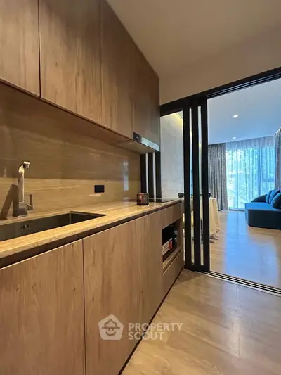 Modern kitchen with wooden cabinets and open layout leading to a bright living area.