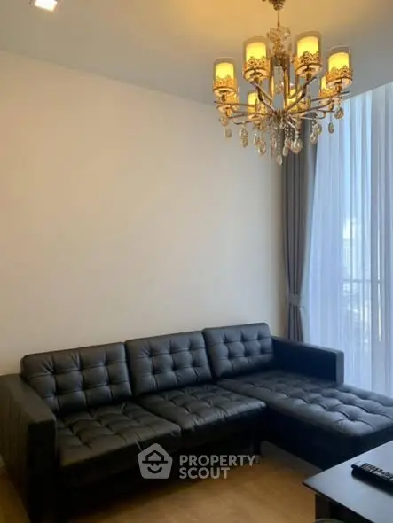Modern living room with elegant chandelier and black leather sectional sofa.