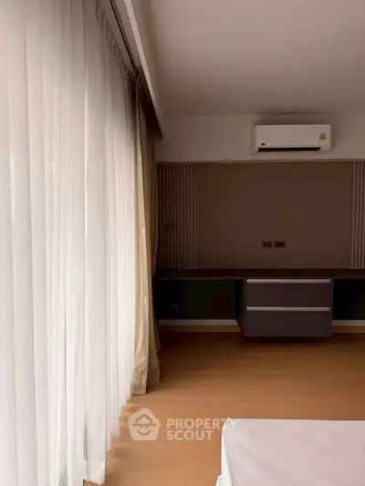 Spacious bedroom with large windows and modern air conditioning unit, offering ample natural light and comfort.