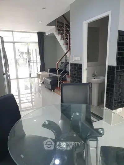 Modern open-plan living area with glass dining table and sleek staircase