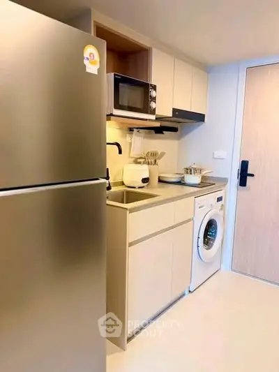 Modern compact kitchen with fridge, microwave, and washing machine in sleek apartment.