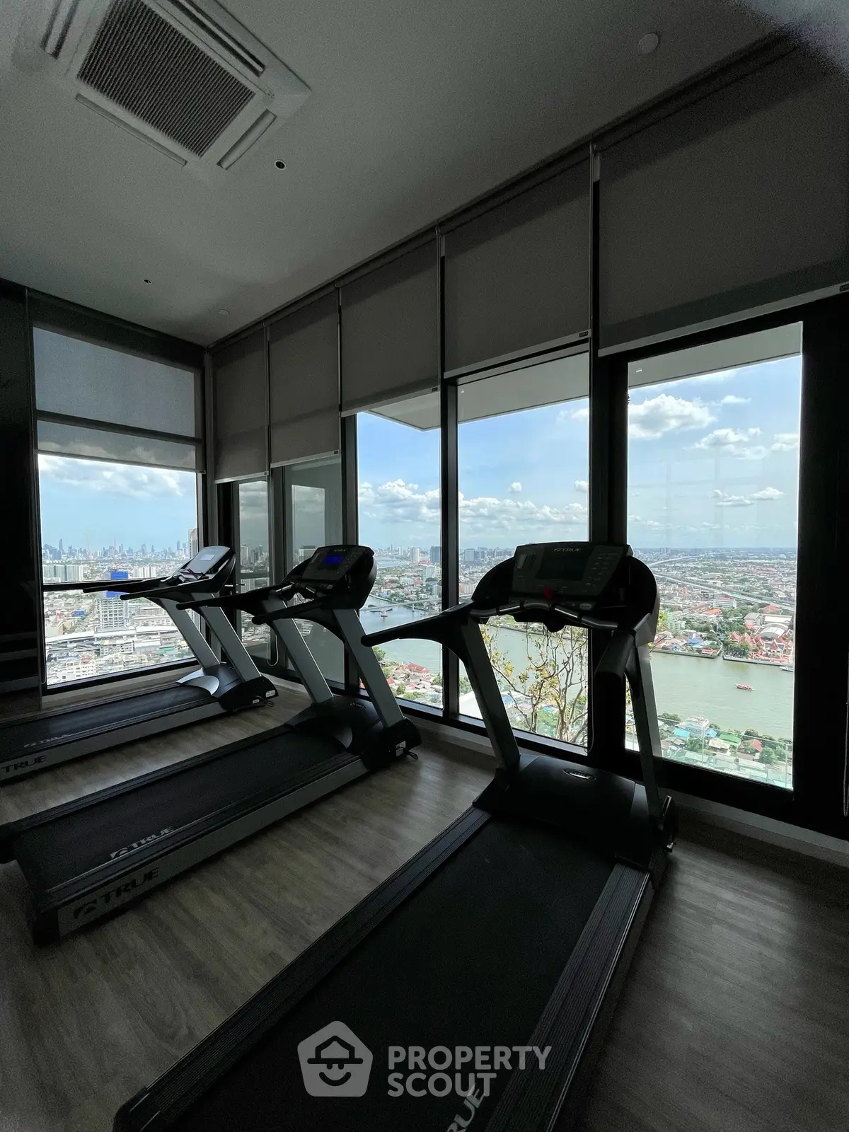 High-rise gym with panoramic city and river views, featuring modern treadmills and floor-to-ceiling windows.