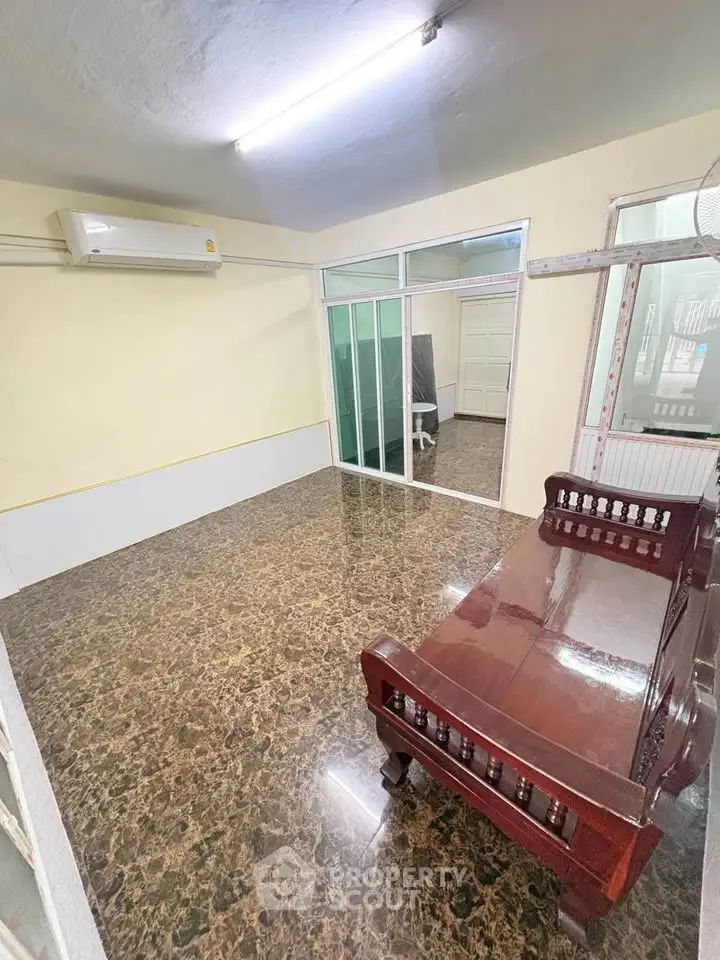 Spacious living room with elegant wooden furniture and marble flooring, featuring air conditioning and sliding glass doors.