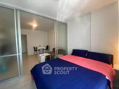 Modern bedroom with sliding glass doors leading to a dining area, featuring a cozy bed with vibrant bedding.