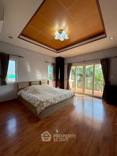 Spacious bedroom with wooden flooring and balcony access, featuring large windows for natural light.