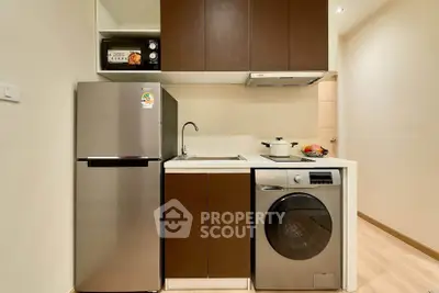 Modern compact kitchen with stainless steel fridge and washing machine in cozy apartment.