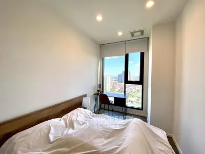 Bright bedroom with city view, featuring a cozy bed and a work desk by the window.