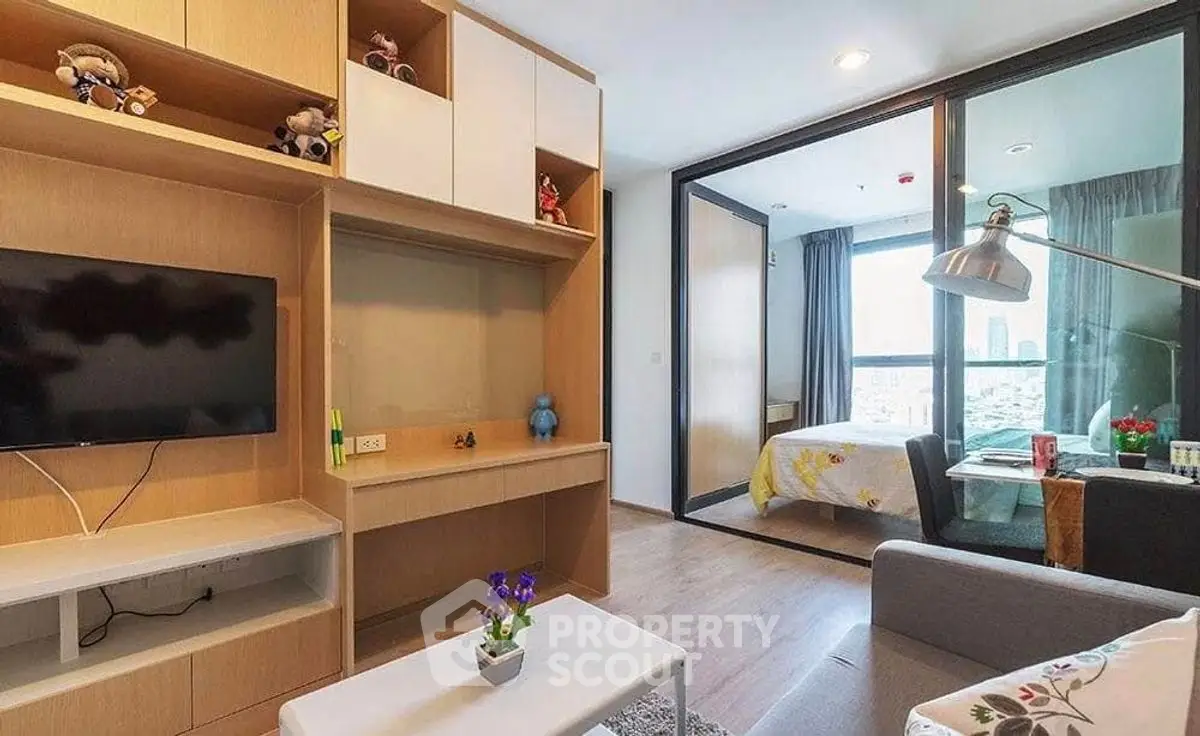 Modern living room with TV and view into bedroom, featuring stylish decor and natural light.
