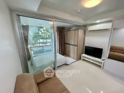 Modern bedroom with glass partition and cozy living area, featuring sleek furniture and natural light.