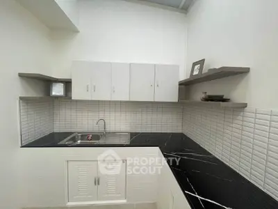 Modern kitchen with sleek black countertops and white cabinetry, featuring open shelving and stylish backsplash.