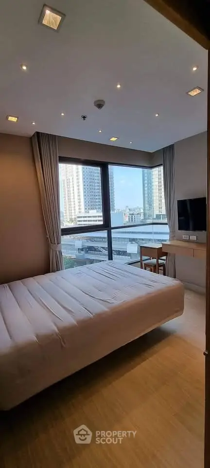 Modern bedroom with large window offering city view, featuring cozy bed and wall-mounted TV.