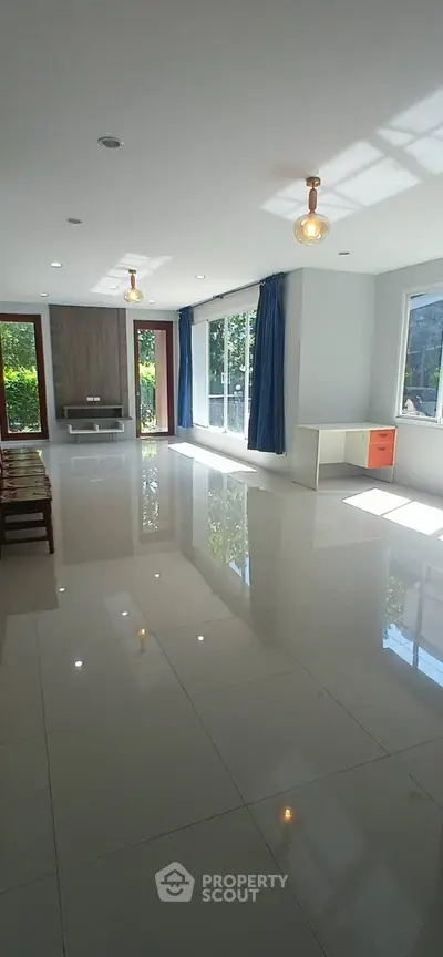 Spacious living room with large windows and glossy tile flooring, offering abundant natural light and garden views.