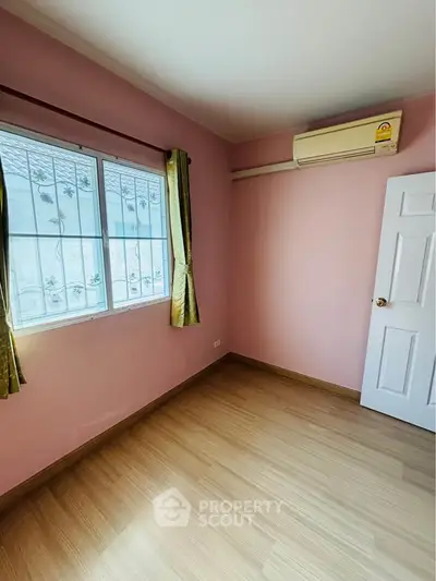 Charming bedroom with pink walls, wooden flooring, and air conditioning unit.