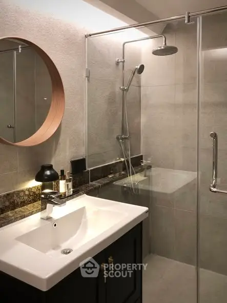 Modern bathroom with glass shower, round mirror, and stylish sink in elegant design.