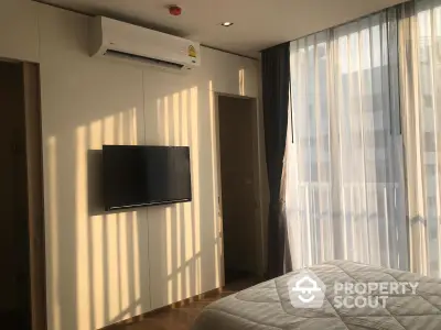 Sun-drenched modern bedroom with wall-mounted TV, sheer curtains, and a cozy ambiance, perfect for relaxation and comfort.