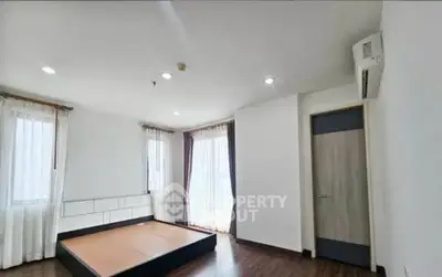 Spacious bedroom with wooden flooring and large windows for natural light.