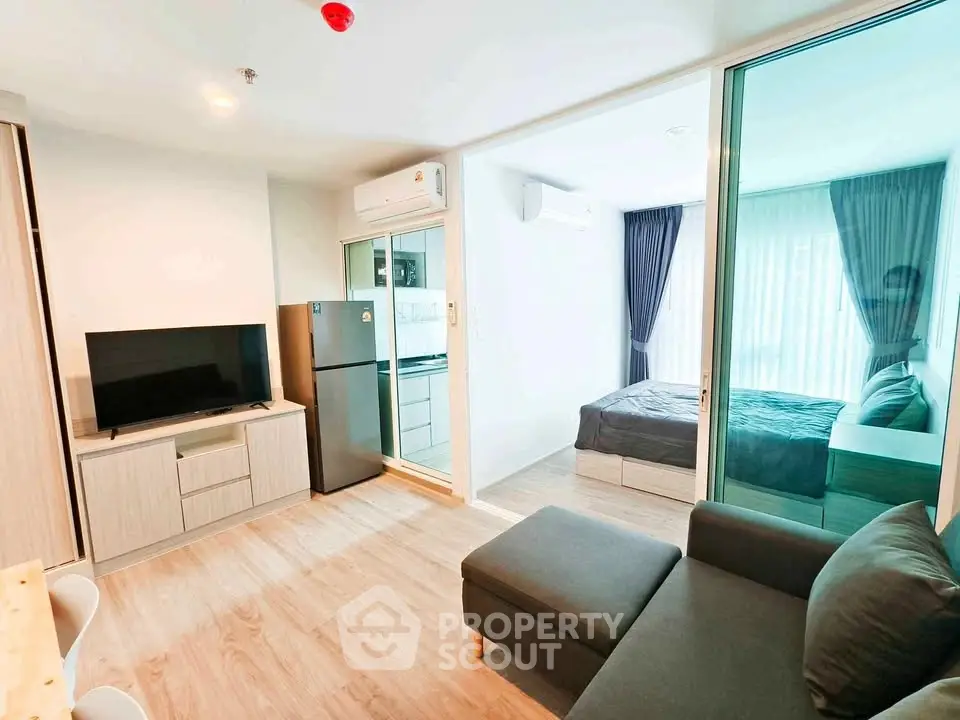 Modern living room with open layout and bedroom view, featuring sleek furniture and natural light.