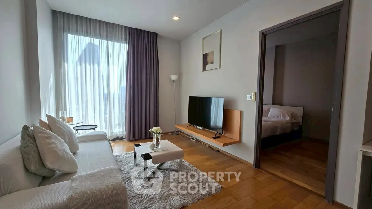 Modern living room with cozy sofa, TV, and natural light from large window.