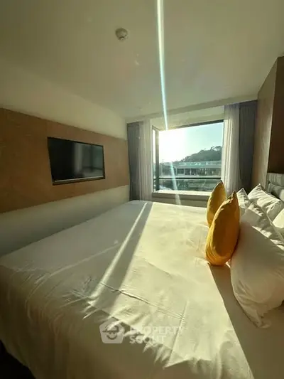 Bright bedroom with large window and modern decor, featuring a comfortable bed and wall-mounted TV.