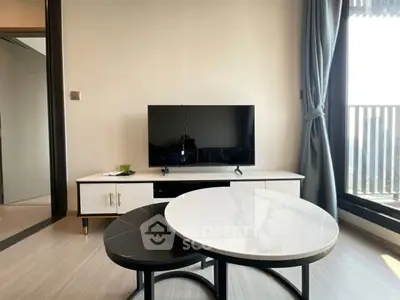 Modern living room with sleek TV setup and stylish coffee tables near balcony.