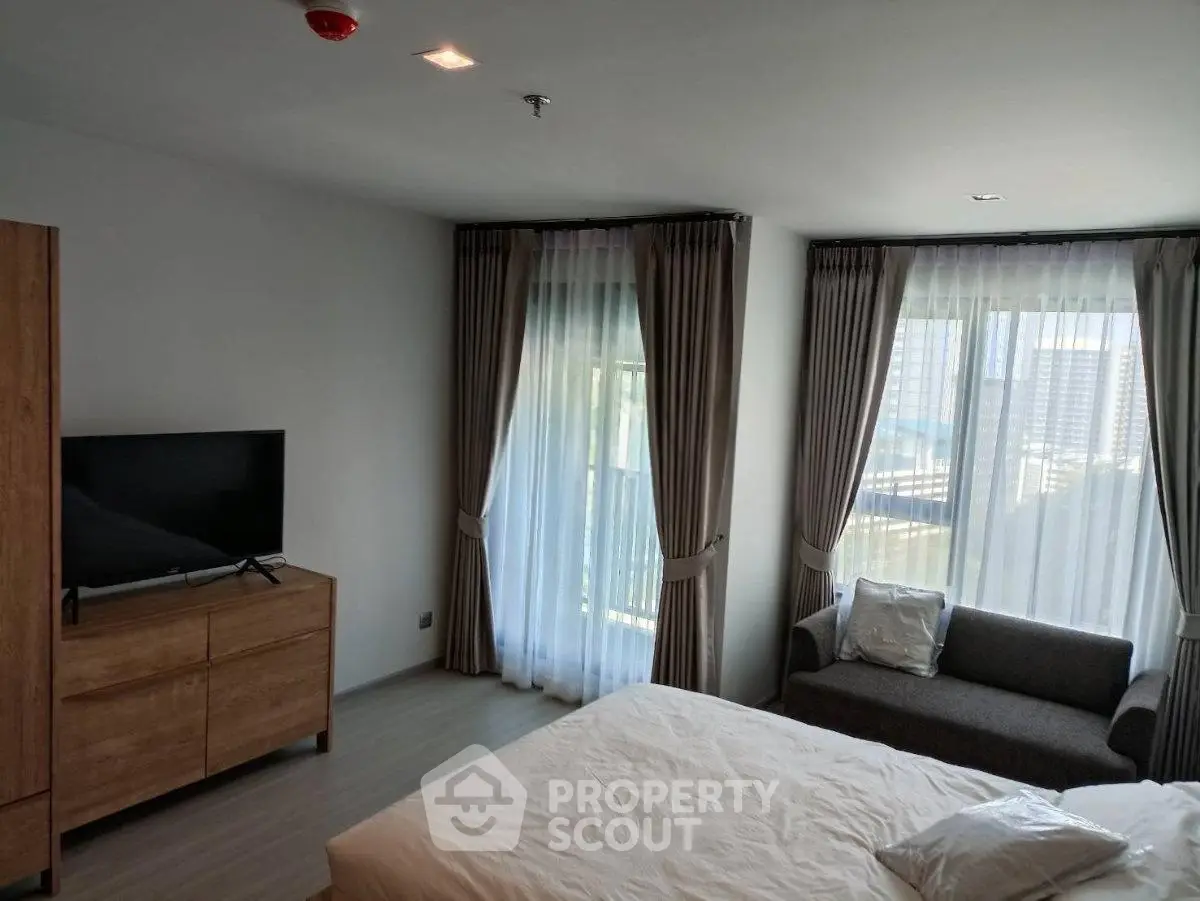 Spacious bedroom with large windows and modern furnishings in a high-rise apartment.