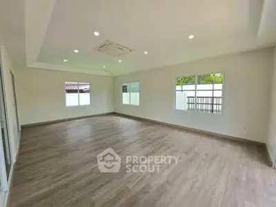 Spacious empty room with wooden flooring and large windows, perfect for customization.