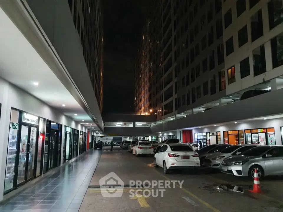 Modern commercial building exterior with parking area at night, showcasing retail spaces and parked cars.