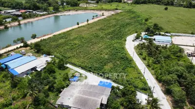 Aerial view of expansive green land with adjacent water body and nearby structures, ideal for development.