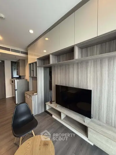 Modern living room with sleek TV unit and compact kitchen in open layout apartment.
