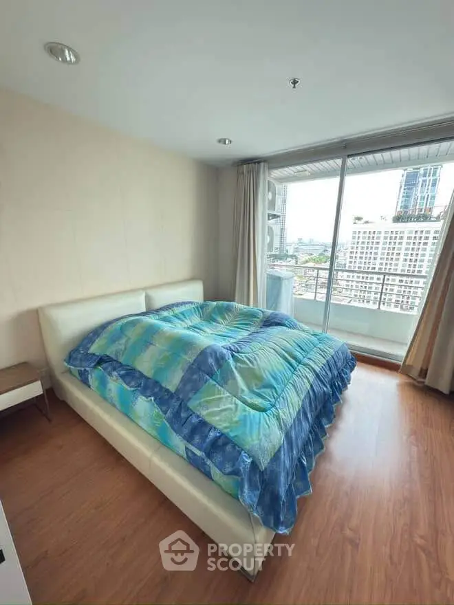 Spacious bedroom with large window and city view, featuring modern decor and wooden flooring.