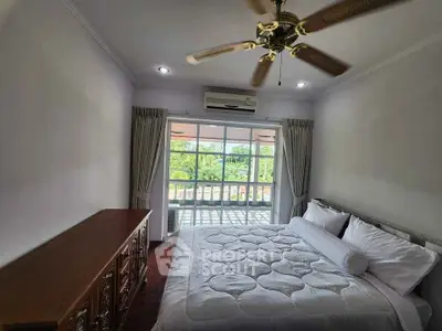 Cozy bedroom with large window and ceiling fan, offering a serene view and ample natural light.
