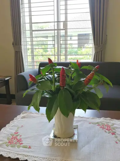 Cozy living room with elegant sofa and vibrant potted plant near a sunlit window.