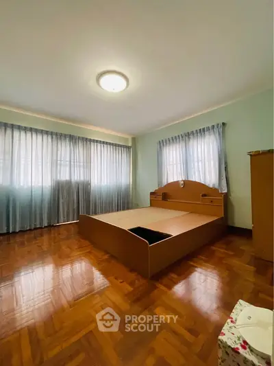 Spacious bedroom with wooden flooring and large windows for natural light.