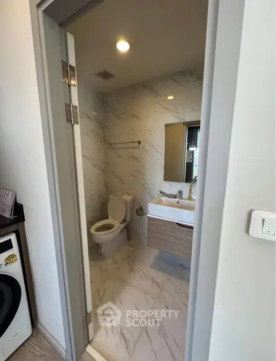 Modern bathroom with marble tiles and washing machine in compact space.
