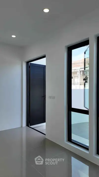 Modern minimalist interior with sleek black door and large windows, offering ample natural light.