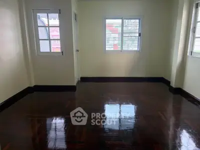 Spacious empty room with polished wooden floors and ample natural light from multiple windows.
