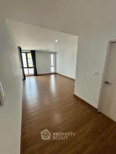 Spacious empty living room with wooden flooring and large windows for natural light.