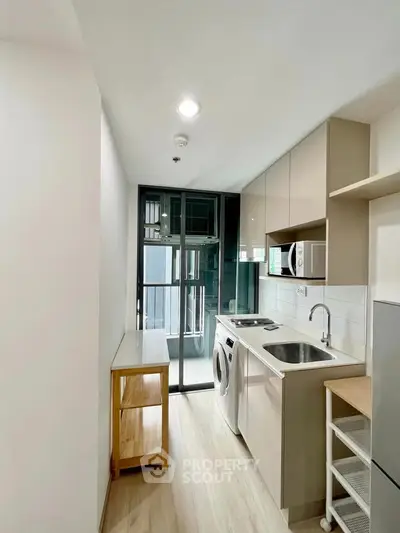 Modern compact kitchen with washing machine and sleek cabinetry in a bright apartment.