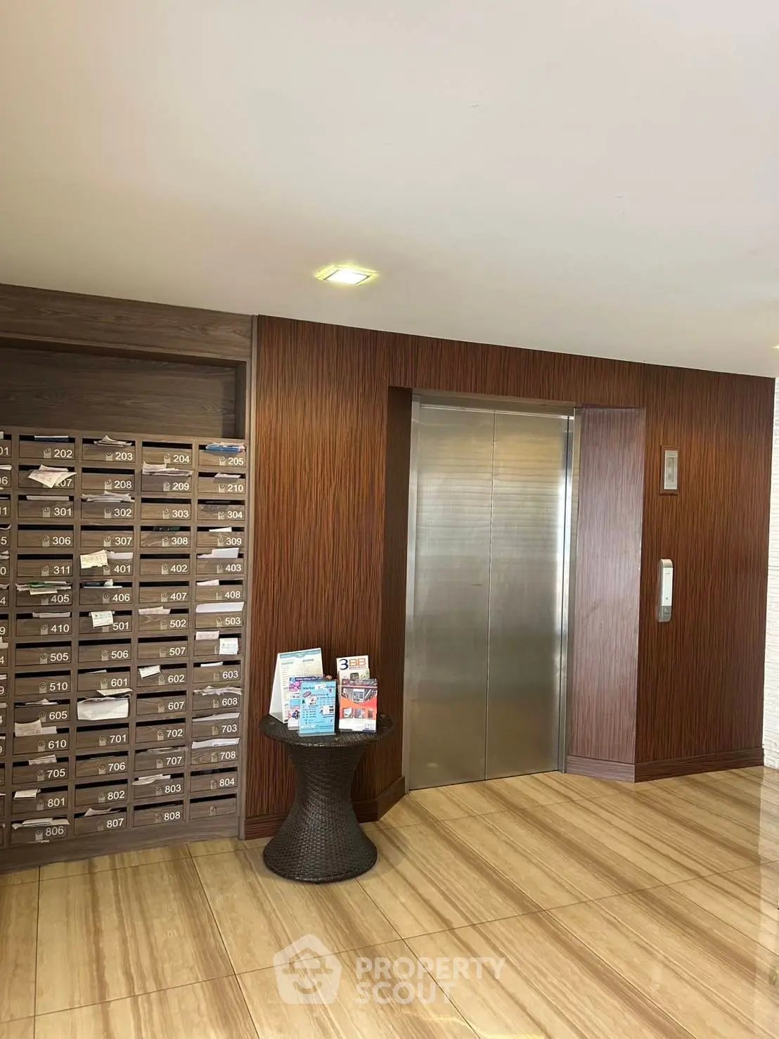 Modern building lobby with elevator and mailboxes, featuring elegant wood paneling and tiled flooring.