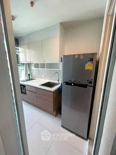 Modern kitchen with sleek cabinets and stainless steel fridge in compact layout.