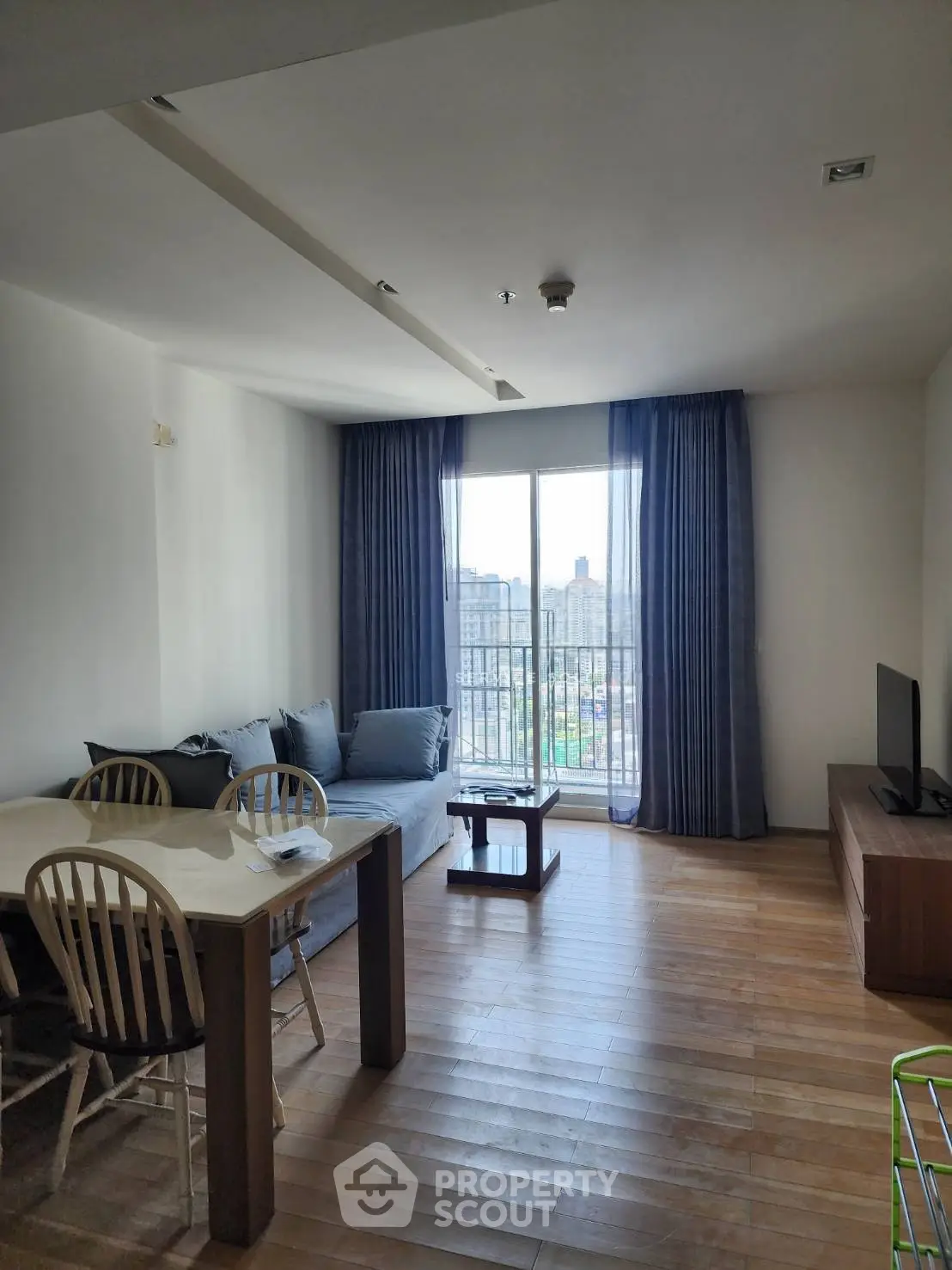 Modern living room with wooden flooring, cozy sofa, dining table, and balcony view.
